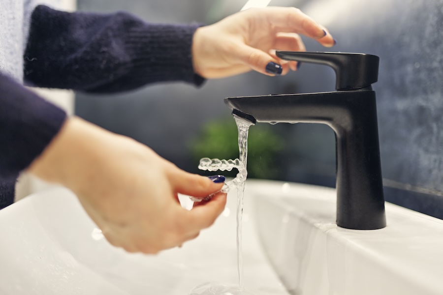 woman caring for invisalign aligners by rinsing them with water in sink